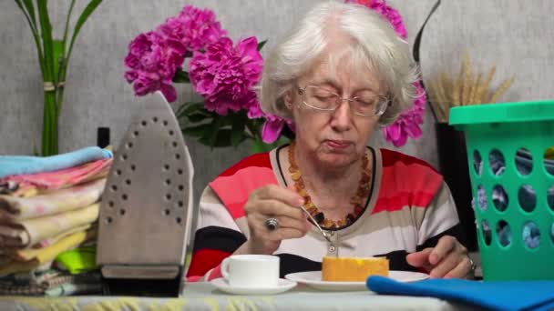 Ederly vrouw taart eten en drinken koffie in de buurt van strijkplank — Stockvideo