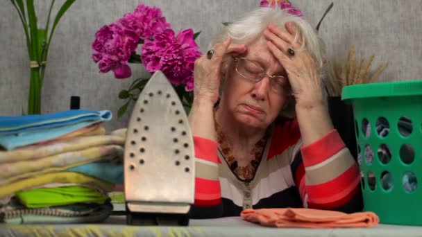Пожилая женщина с головной болью возле гладильной доски — стоковое видео
