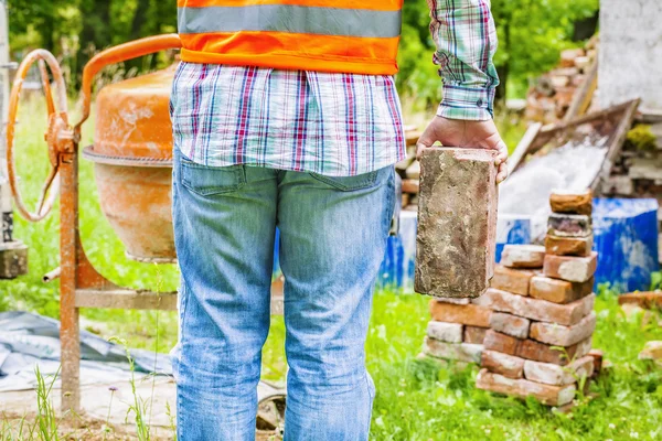 Trabalhador da construção civil com tijolo perto do betoneira — Fotografia de Stock