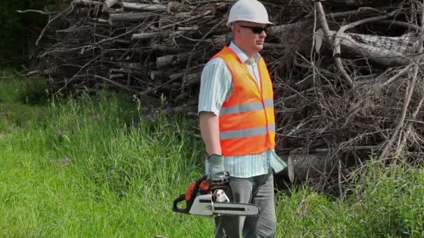 Angry Lumberjack with chainsaw talking near the pile of branches — Stock Video