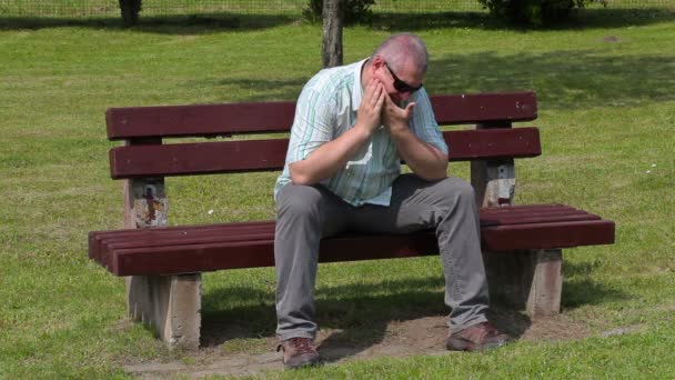 Stressful man with tooth pain in the park on bench — Stock Video