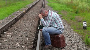 Bavul yakınındaki demiryolu üzerinde oturan stresli adam 