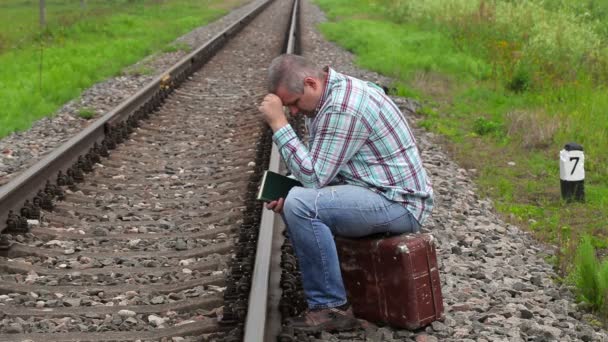 Stressful man sitting on suitcase near railway — Stock Video