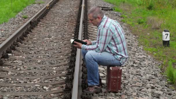 Чоловік сидить на валізі і читає книгу біля залізниці — стокове відео