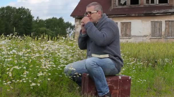 Man zittend op koffer en praten over de telefoon in de buurt van kamille bloemen — Stockvideo