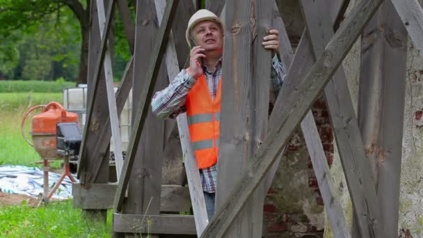 Trabajador de la construcción hablando por teléfono y mirando a través de andamios — Vídeos de Stock