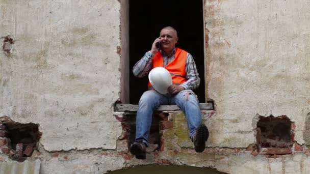 Construction worker sitting in window and talking on phone — Stock Video