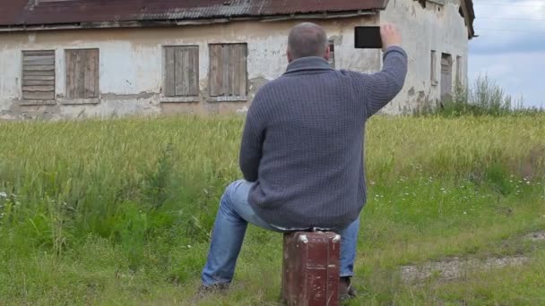 Homem sentado na mala e tirar fotos de casa velha — Vídeo de Stock