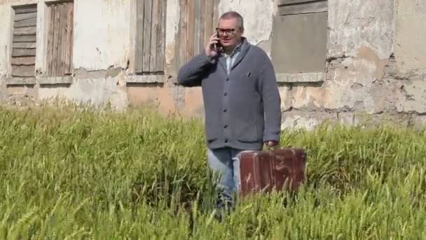 Hombre en el campo con maleta hablando por teléfono — Vídeos de Stock