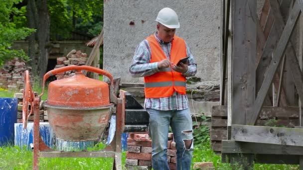 Construction worker checking concrete mixer near wooden scaffolding — Stock Video