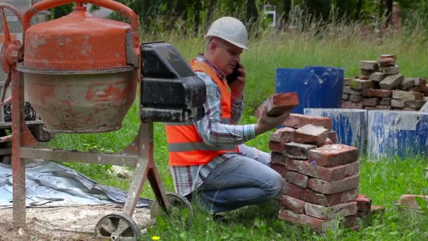 건설 노동자 오래 된 벽돌을 확인 하 고 콘크리트 믹서 근처 스마트 폰 이야기 — 비디오