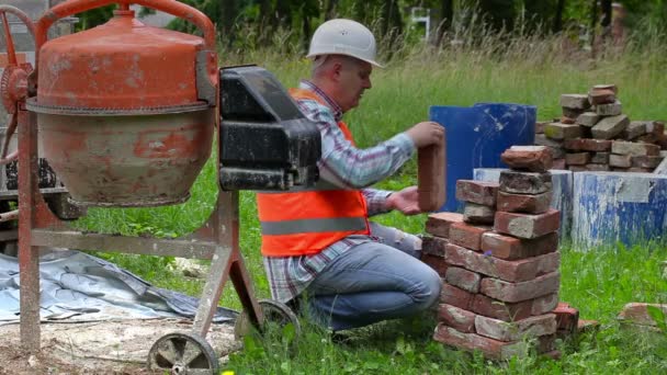 Construction worker sorting old bricks near concrete mixer — Stock Video