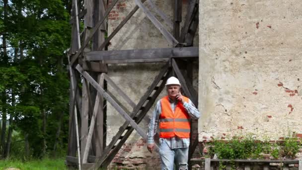 Trabalhador da construção andando e falando no telefone inteligente perto de andaimes de madeira — Vídeo de Stock