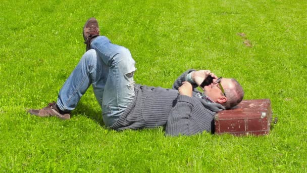 Mann mit Koffer schläft im Gras und telefoniert mit Smartphone — Stockvideo