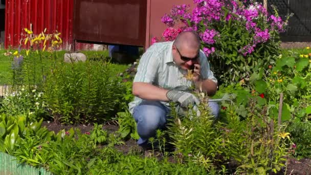 Mężczyzna rozmawia przez telefon w ogrodzie w pobliżu kwiaty — Wideo stockowe