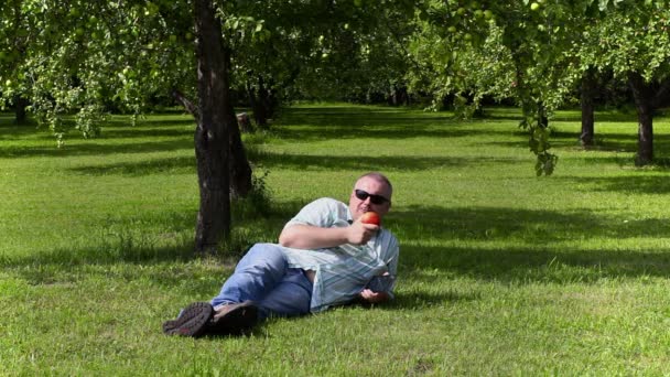 リンゴの果樹園で横になっているリンゴを食べる男 — ストック動画