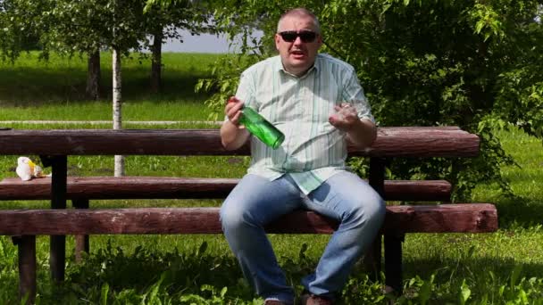 Злой человек с бутылкой алкоголя сидит и разговаривает — стоковое видео