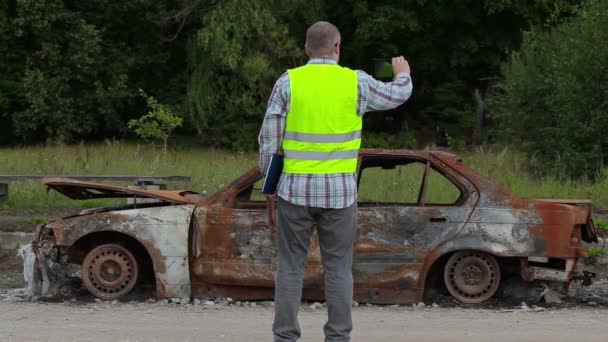 Inspektor robić zdjęcia spalony wrak samochodu na poboczu drogi — Wideo stockowe