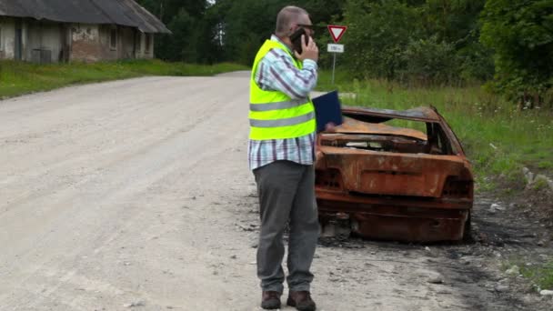 Inspektor läuft in der Nähe des Autowracks und telefoniert mit Smartphone — Stockvideo