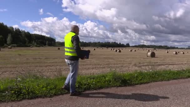 Фермер разговаривает по смартфону и уходит по дороге возле соломенных тюков — стоковое видео