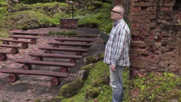 Mannen med Bibeln ser att himlen i utomhus kyrka — Stockvideo