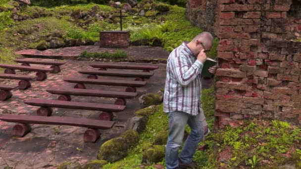 Чоловік плаче біля стіни у старій церкві на відкритому повітрі — стокове відео