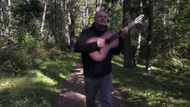 Gelukkig man gitaar spelen en wandelen in het park — Stockvideo