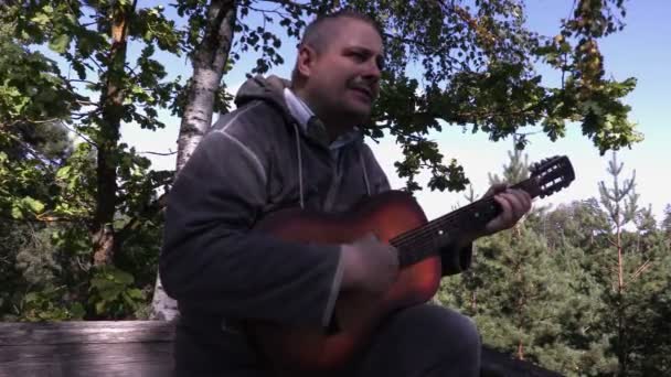 Uomo che suona la chitarra nella torre di legno vicino agli alberi — Video Stock