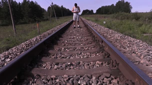 Tiener luisteren naar muziek en wandelen per spoor — Stockvideo