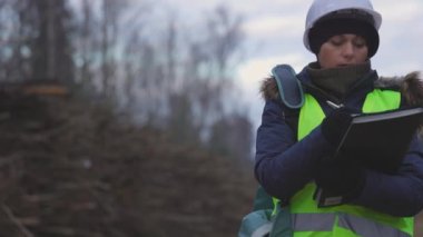  Kadın orman çalışanı yakacak odun yığınlarının yanında yazıyor.