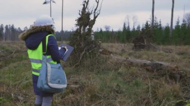 Kadın mühendis ormandaki devrilmiş bir ağacın köklerinde yazıyor.