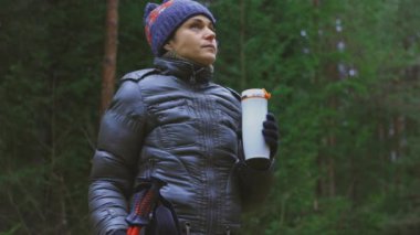 Kadın yürüyüşçü orman yolunda duruyor ve çay ya da kahve içiyor.