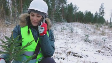 Genç ladin yakınında telefonla konuşan mutlu kadın orman bilimcisi.