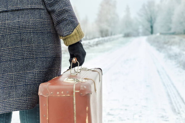 Woman with vintage suitcase walking on road in winter