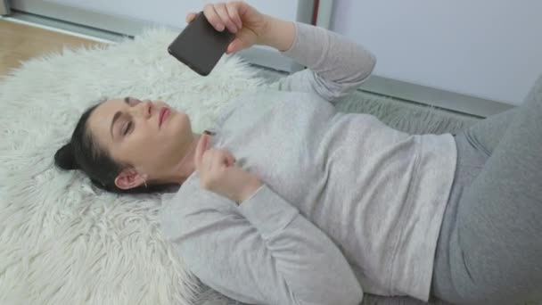 カーペットの上に横たわっている間 スマートフォンを使って幸せな女性 — ストック動画