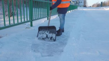Kadın hademe kar küreğiyle karları kaldırıyor.