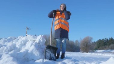 Kar küreği tutan ve telefonla konuşan kadın hademe.