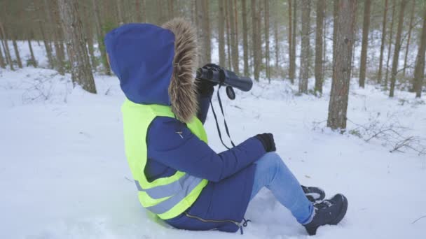 女人坐在雪地上透过双筒望远镜看森林 — 图库视频影像