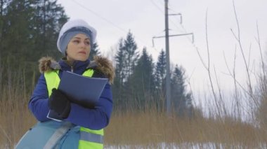 Kadın elektrik mühendisi yüksek voltaj hattının altındaki notları yazıyor.