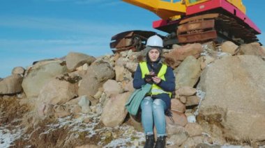 Güvenlik mühendisliği taş üstünde oturuyor ve kazıcının yanındaki dizüstü bilgisayarda çalışıyor.