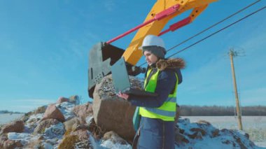 Kazı makinesinin yanında dizüstü bilgisayar kullanan kadın mühendis.