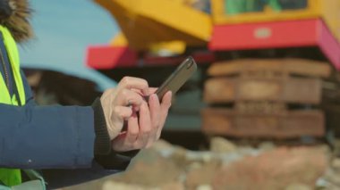 Sürüngen traktörünün yanında akıllı telefon kullanan kadın mühendis.