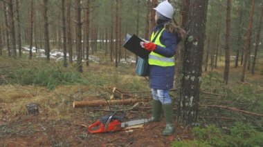 Ormandaki ağacın yanında kitap okuyan kadın orman işçisi.