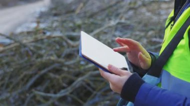 Kadın mühendis, kesik dalların yanında tablet kullanıyor