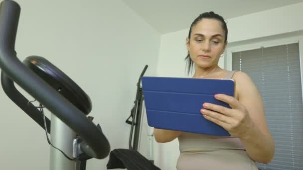 Donna Che Utilizza Tablet Allenamento Sulla Cyclette Casa — Video Stock