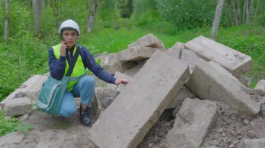 Kadın inşaat mühendisi telefonda konuşuyor. Orman yolundaki beton blokların yanında.