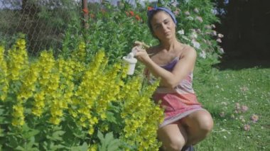 Kadın bahçıvan çiçeklere böcek ilacı sıkıyor.