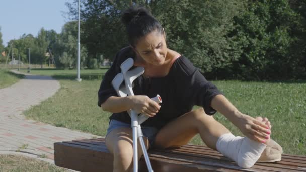 Женщина Держит Костыли Осматривает Поврежденную Ногу — стоковое видео