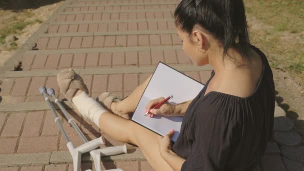 Niepełnosprawna Kobieta Kulami Siedząca Schodach Rysująca Notatniku — Wideo stockowe