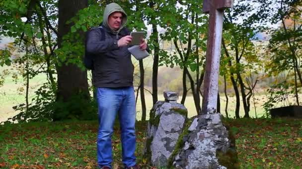 Wandelaar met tablet Pc in de buurt van oude stenen kruisen — Stockvideo